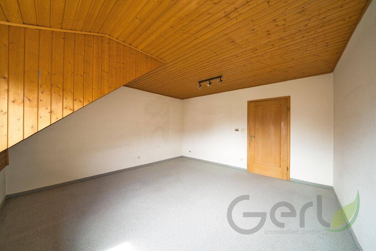 Leerer Dachbodenraum mit Holzverkleidung an der Decke und Teppichboden.