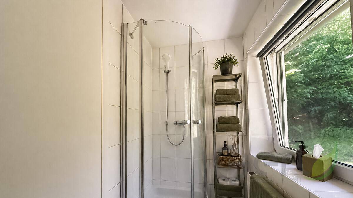 Badezimmer mit Duschkabine, Fenster und Blick ins Grüne für natürliche Belichtung.