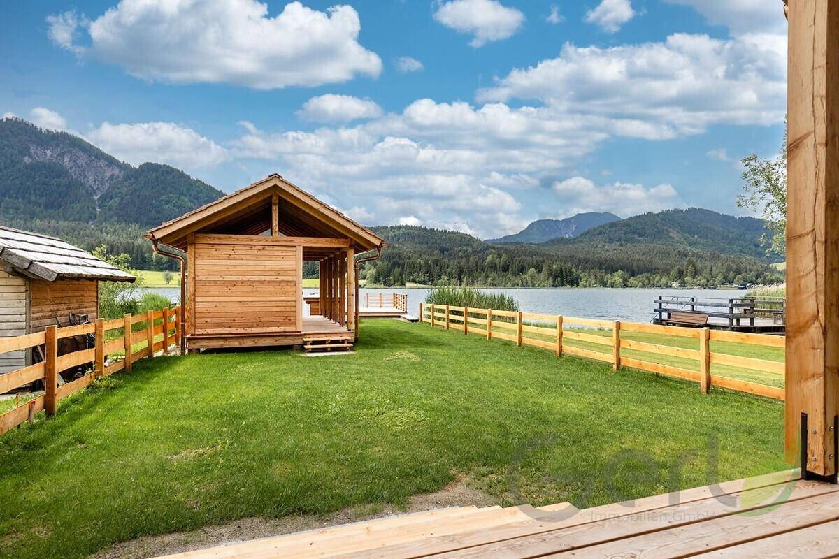 Gepflegter Gartenbereich mit Holzzaun und kleinem Holzhaus, direkt am Seeufer gelegen.