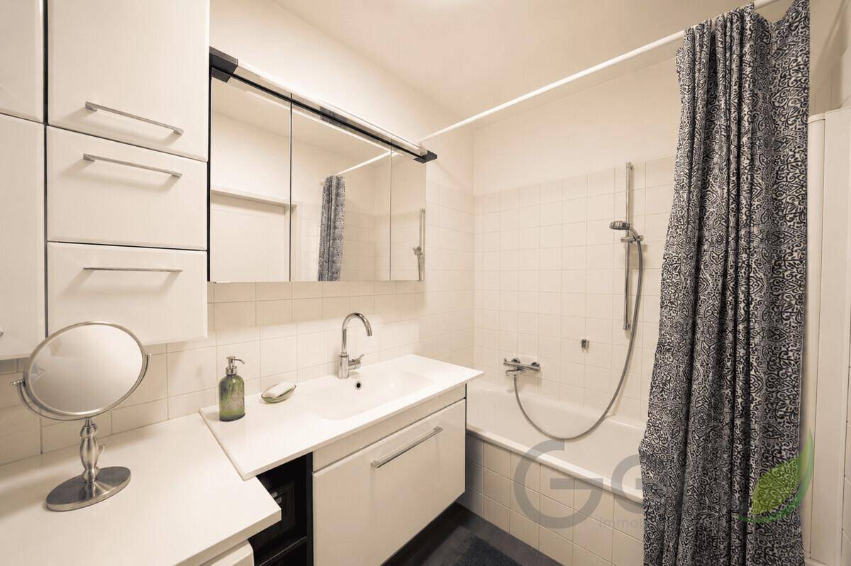 Helles Badezimmer mit Badewanne, Duschvorhang, Waschbecken und Spiegelschrank.
