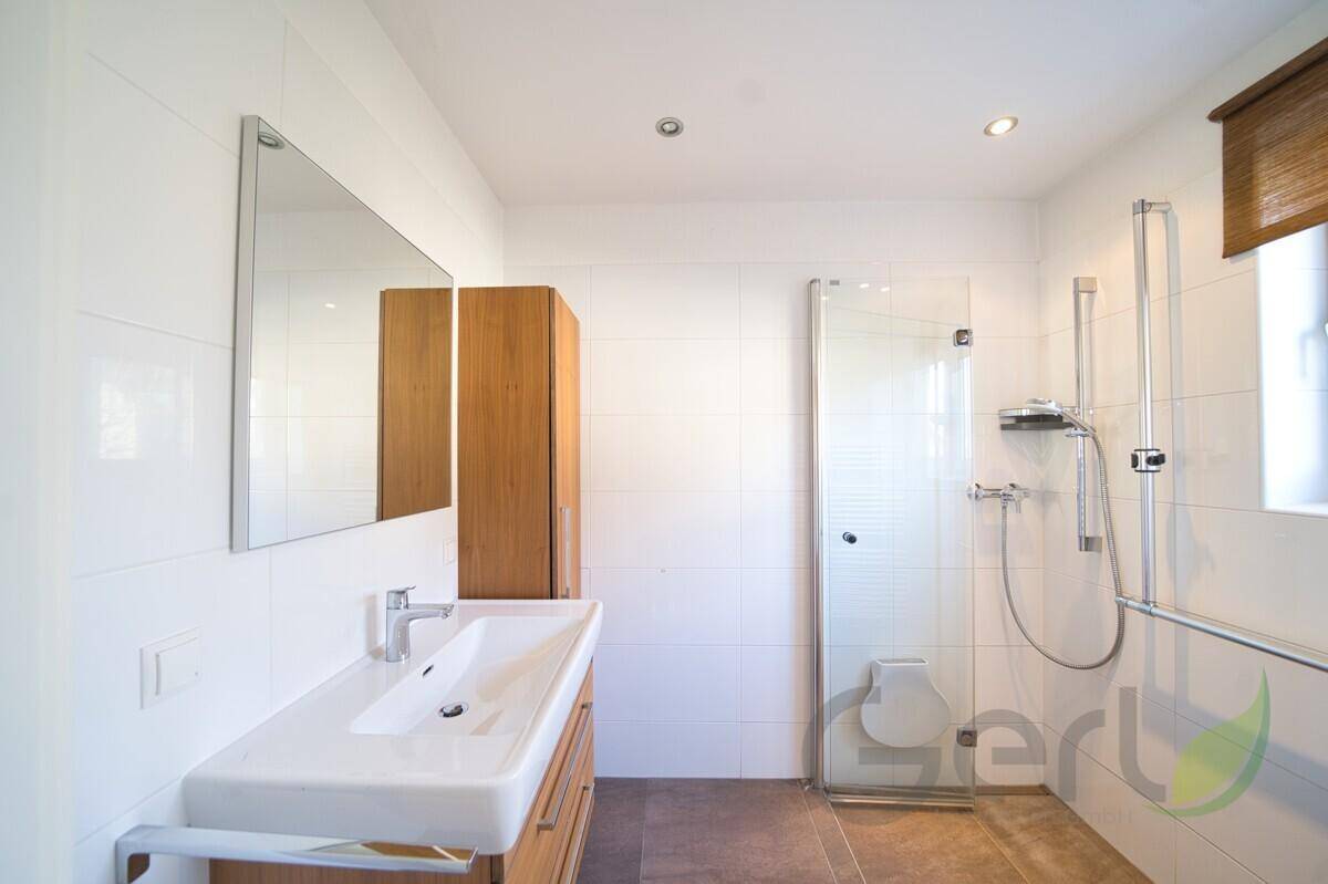 Helles Badezimmer mit Dusche, Einzelwaschbecken, Fenster und Haltegriffen für Komfort.