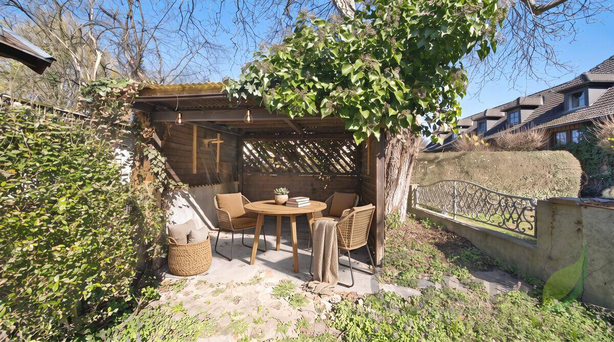 Gemütlicher Sitzbereich im Garten unter einer Holzüberdachung, ideal zum Entspannen.