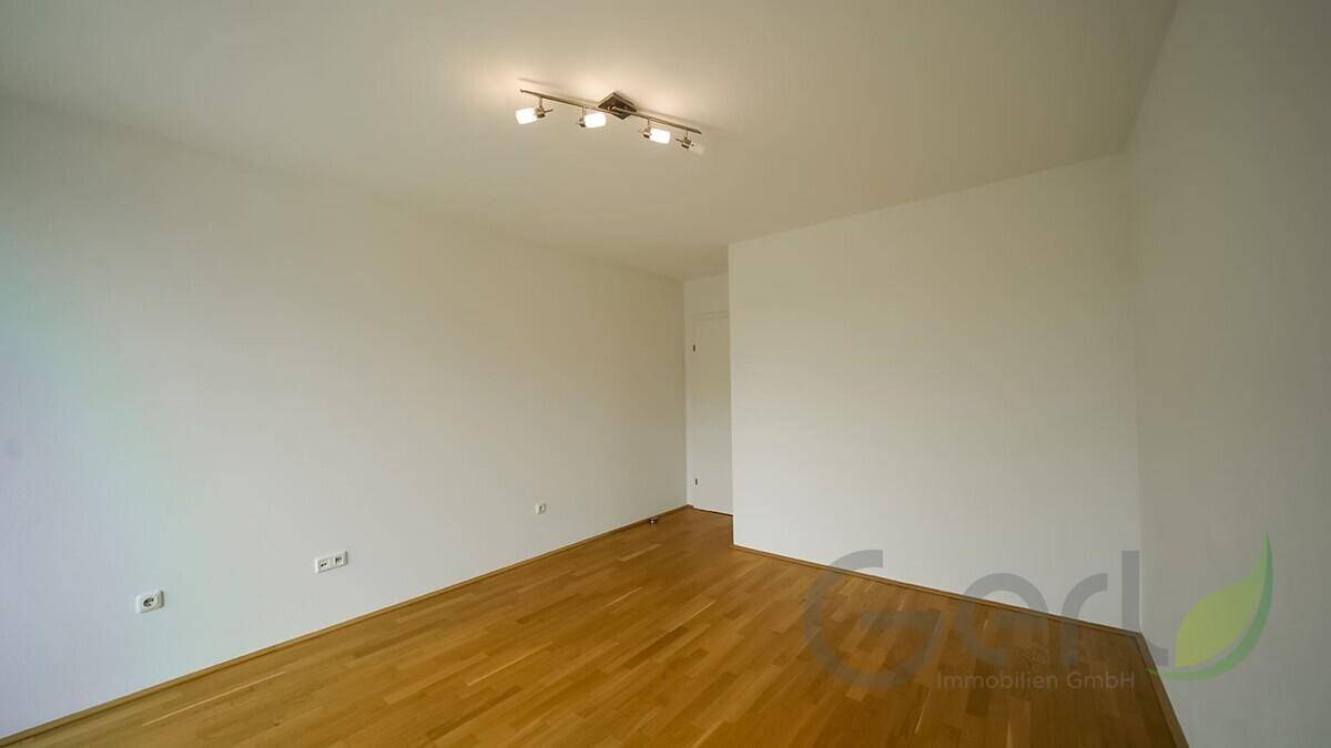 Helles, leeres Zimmer mit warmem Holzfußboden und weißen Wänden, bereit zur individuellen Gestaltung.