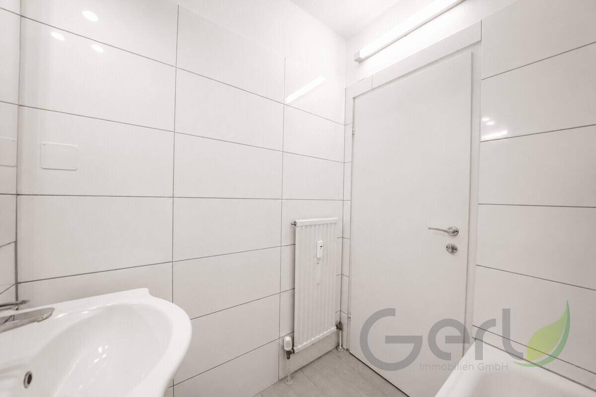 Weiß gefliestes Badezimmer mit Heizkörper und Tür, sauber und funktional gestaltet.