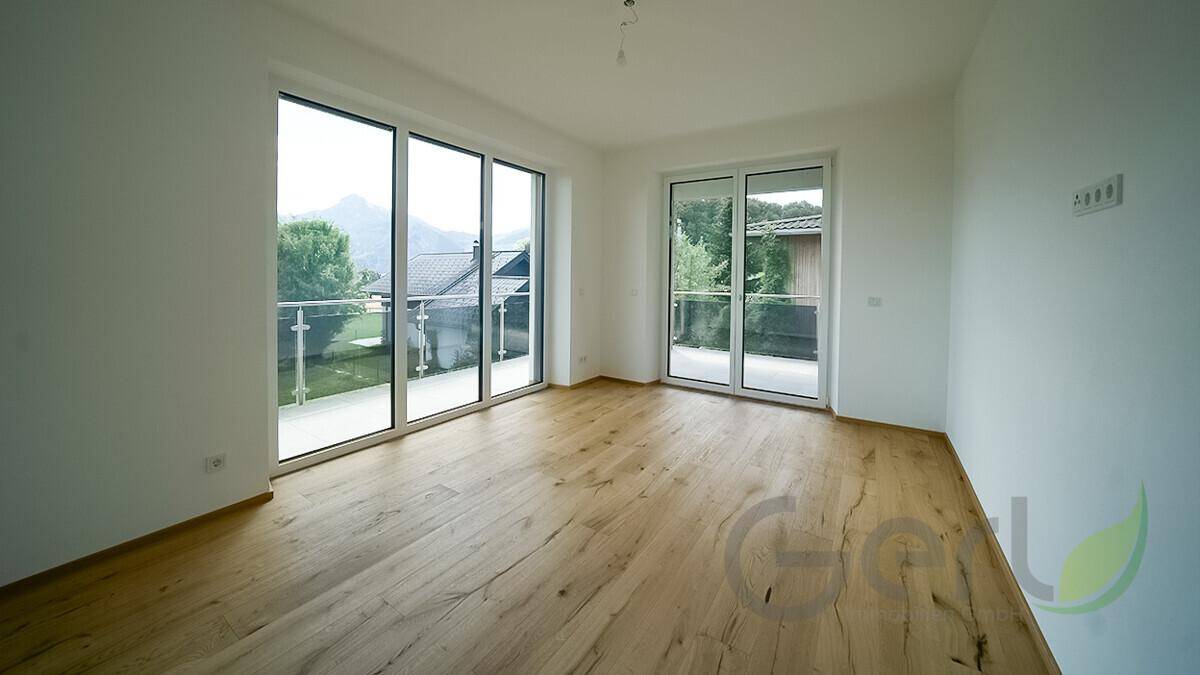 Heller, leerer Raum mit Holzfußboden und großen Glastüren zum Balkon, mit Bergblick.