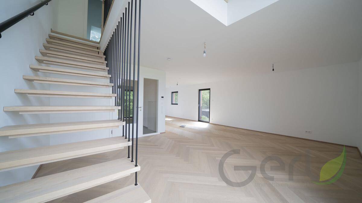 Moderner Treppenaufgang mit Holzstufen und schwarzem Geländer in einem lichtdurchfluteten Wohnbereich.