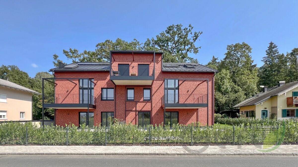 Modernes Mehrfamilienhaus mit roter Ziegelfassade, Balkonen und grüner Hecke.