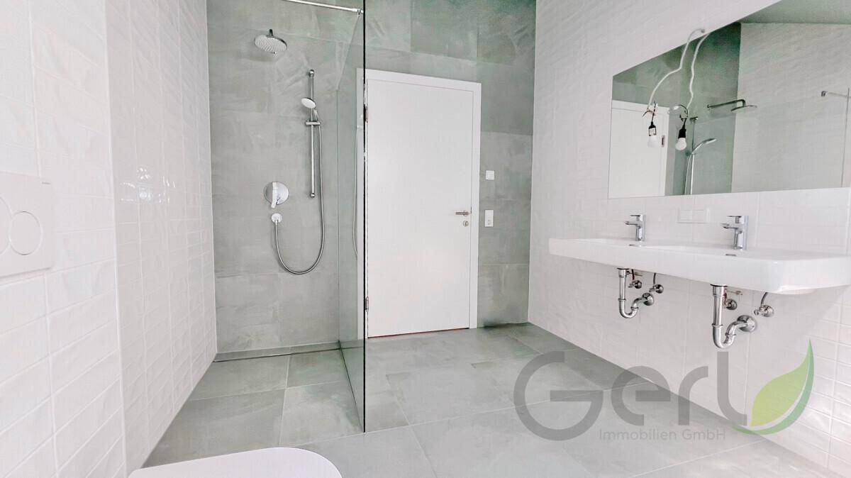 Helles, modernes Badezimmer mit Doppelwaschbecken, begehbarer Dusche und grauen Fliesen.