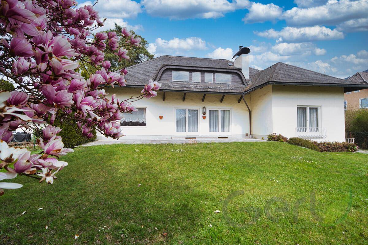 Vorderansicht des Hauses mit gepflegtem Rasen und blühendem Magnolienbaum unter blauem Himmel.