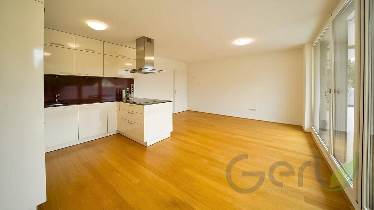 Moderne Einbauküche mit weißen Schränken, Dunstabzugshaube und hellem Holzfußboden, mit Zugang zur Terrasse.