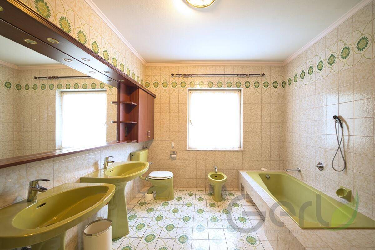 Badezimmer im Stil der 80er Jahre mit grünen Sanitärobjekten und gemusterten Fliesen.