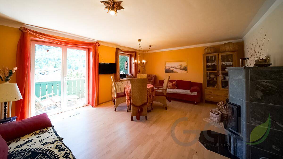 Geräumiger Wohn-Essbereich mit Balkonzugang, traditionellem Kaminofen und heller Wandgestaltung.