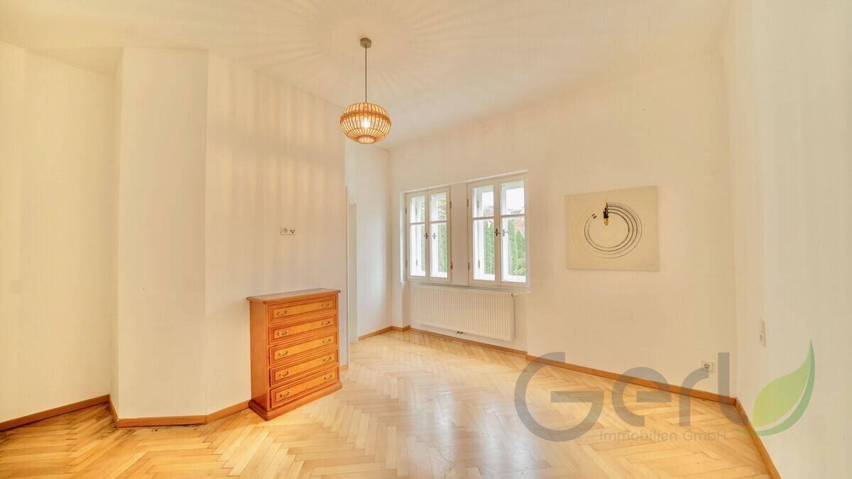 Geräumiges Schlafzimmer mit Fischgrätparkett, Kommode und großen Fenstern.