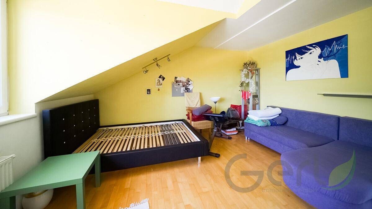 Geräumiges Schlafzimmer im Dachgeschoss mit schräger Decke, Bettrahmen und farbenfroher Gestaltung.