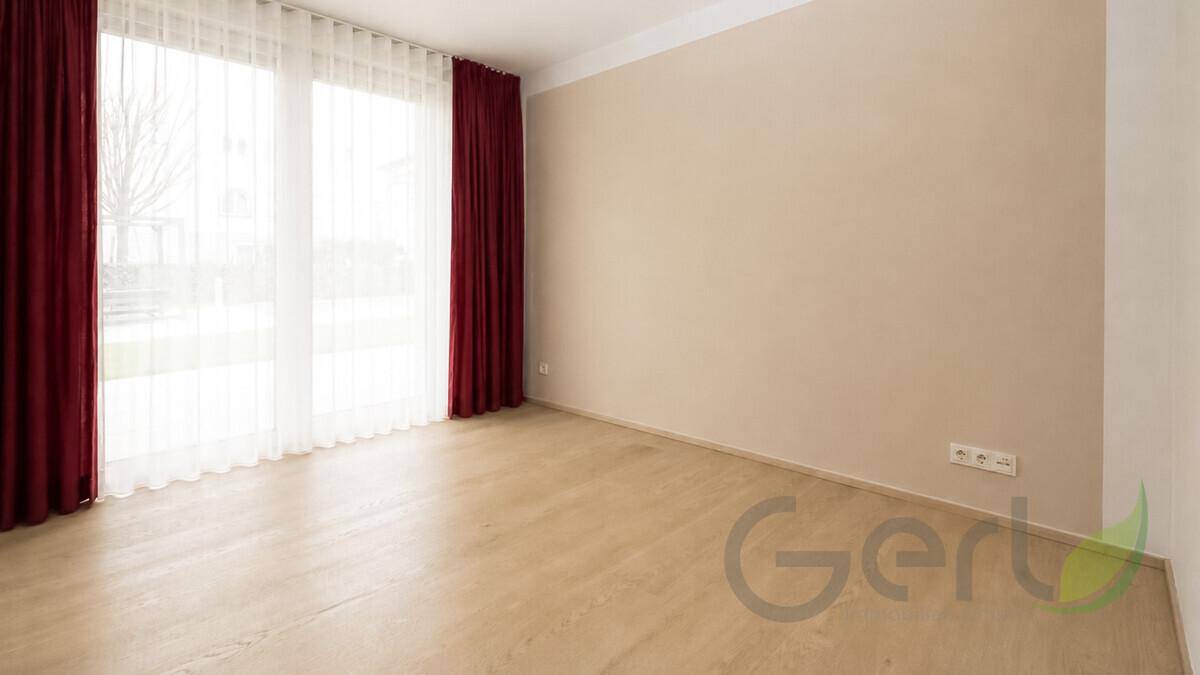 Heller, leerer Raum mit großen Fenstern, hellbraunem Laminatboden und roten Vorhängen.