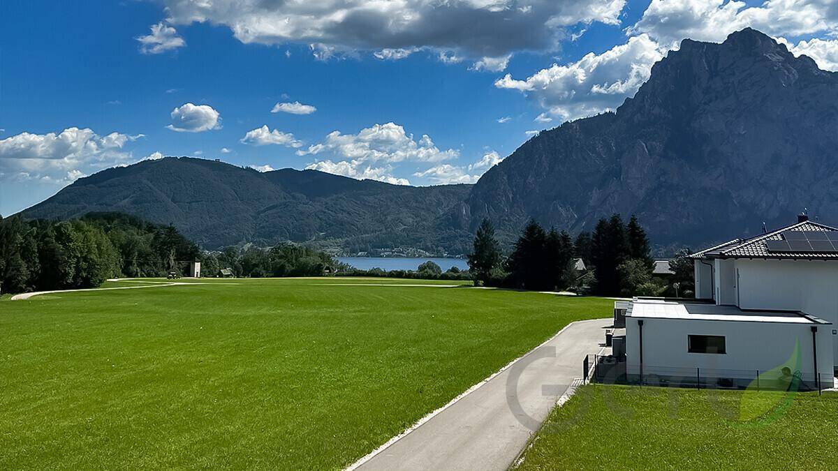 Weitläufige Grünfläche mit Blick auf den See und die majestätischen Berge im Hintergrund.