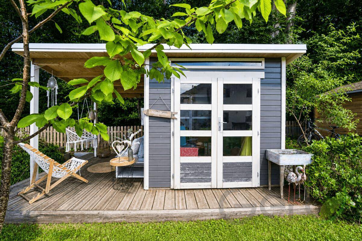 Gemütliches Gartenhaus mit kleiner Holzterrasse und Sitzgelegenheiten im Grünen.