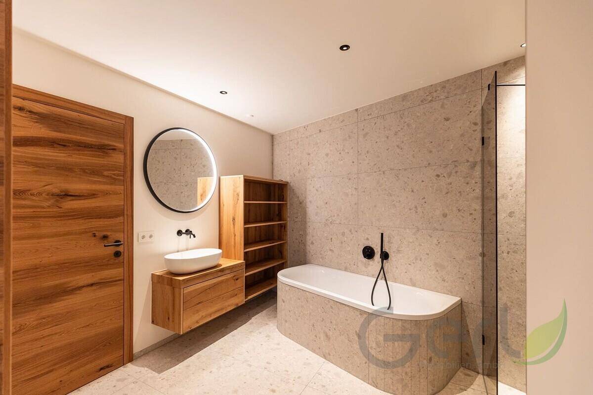 Modernes Badezimmer mit freistehender Badewanne, Holzmöbeln und rundem Spiegel.