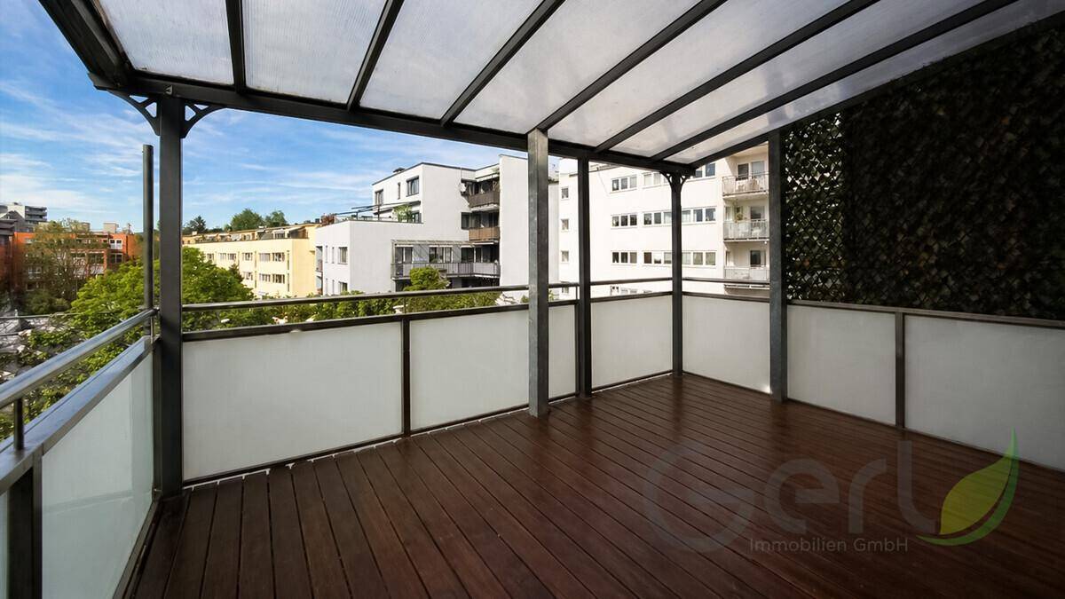Überdachter Balkon mit Holzboden und Blick auf die umliegenden Gebäude an einem sonnigen Tag.