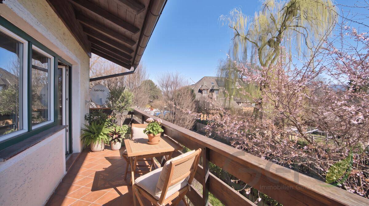 Sonniger Balkon mit Terrakottafliesen und Sitzgelegenheiten, umgeben von blühenden Bäumen.