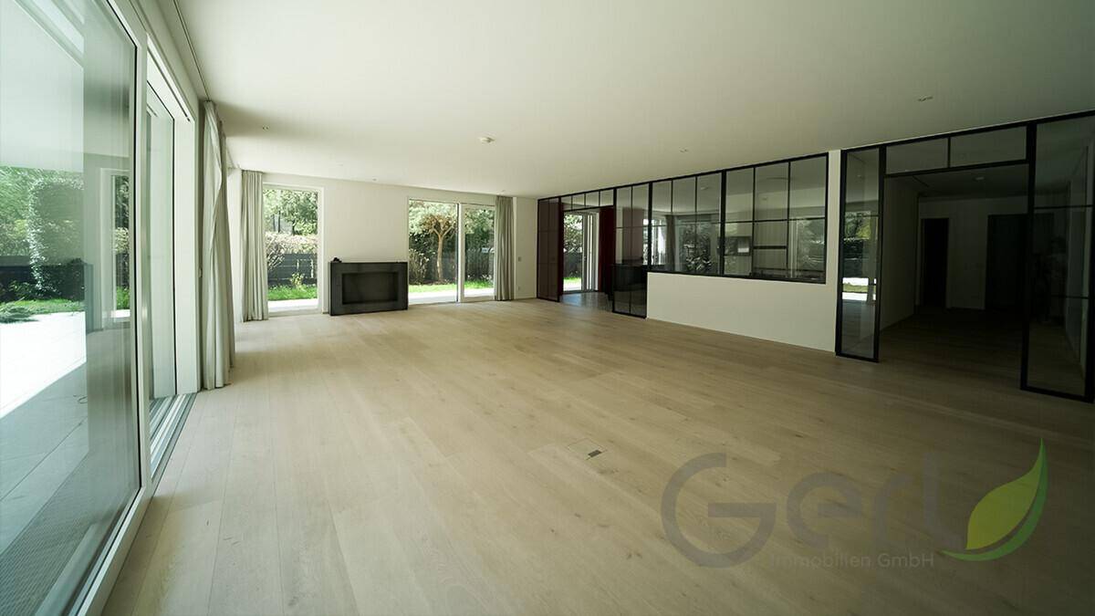 Helles, leeres Wohnzimmer mit Holzboden, großen Fensterfronten und Blick in den Garten.