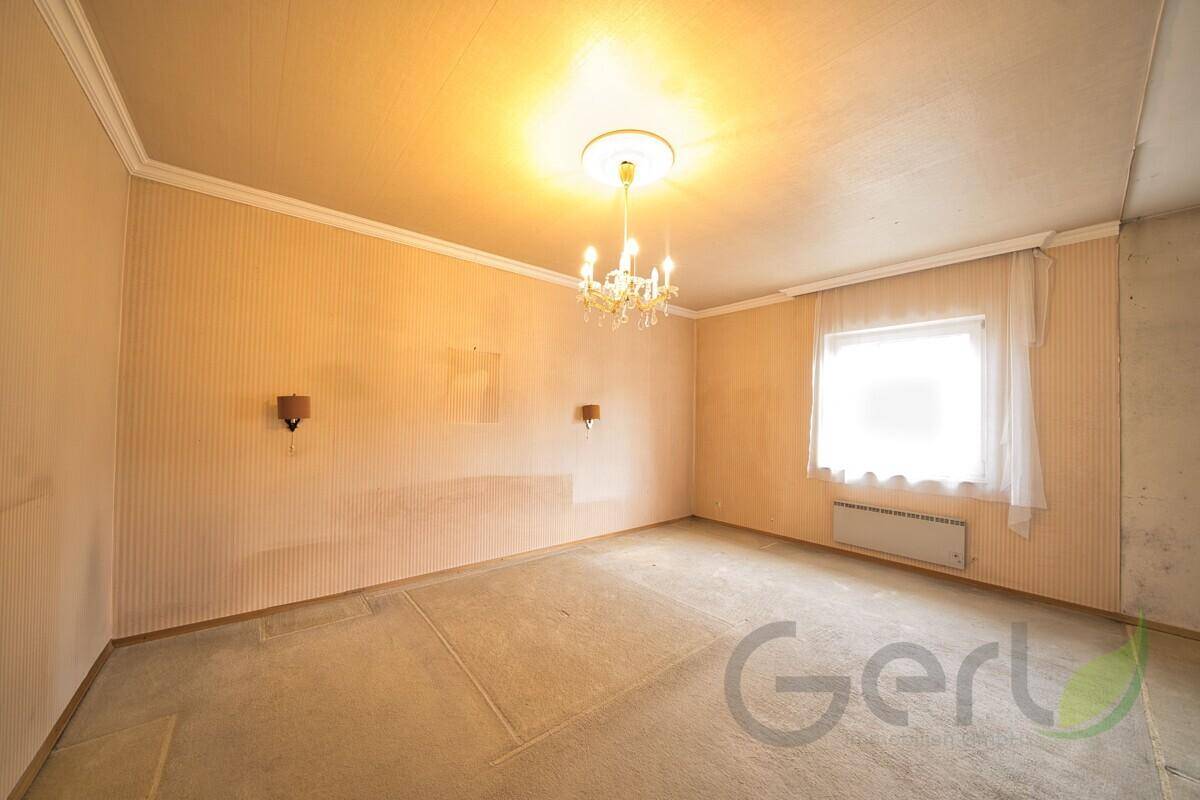 Leeres Schlafzimmer mit Teppichboden, Tapeten und einem Fenster in Originalzustand.