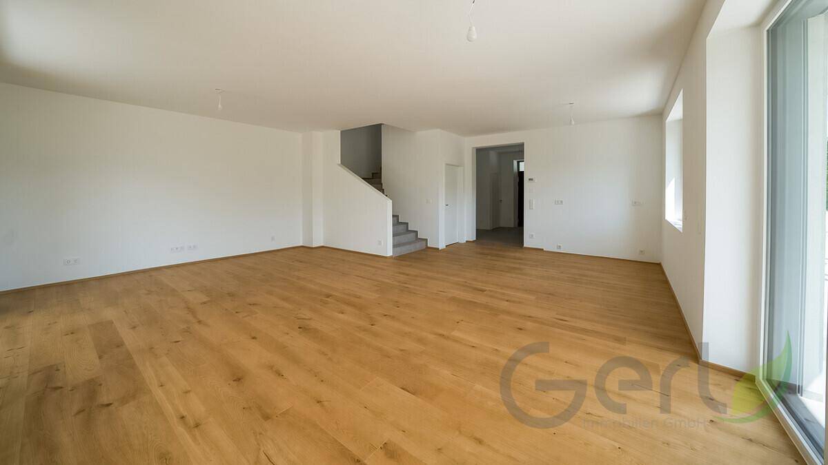 Heller, leerer Raum mit hochwertigem Holzfußboden und Zugang zu großen Fenstern.