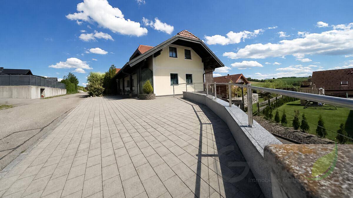 Breite gepflasterte Zufahrt zum Haus mit niedriger Mauer und Geländer, bietet bequemen Zugang.