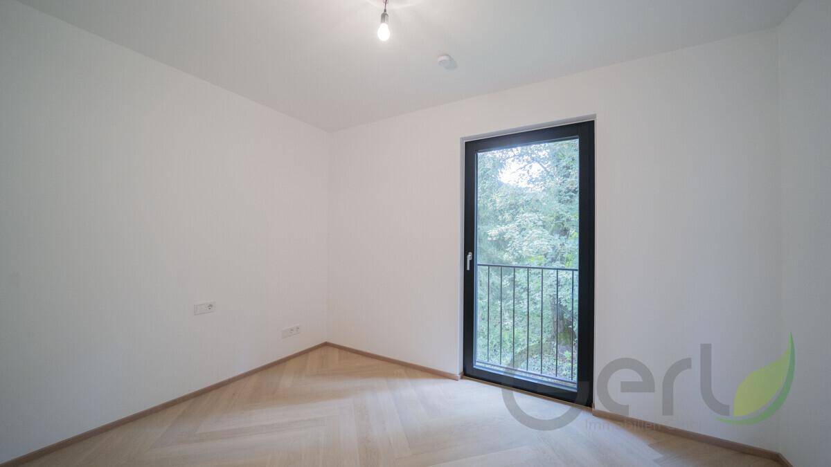 Helles, leeres Schlafzimmer mit Fischgrätparkett und großem Fenster zum französischen Balkon.