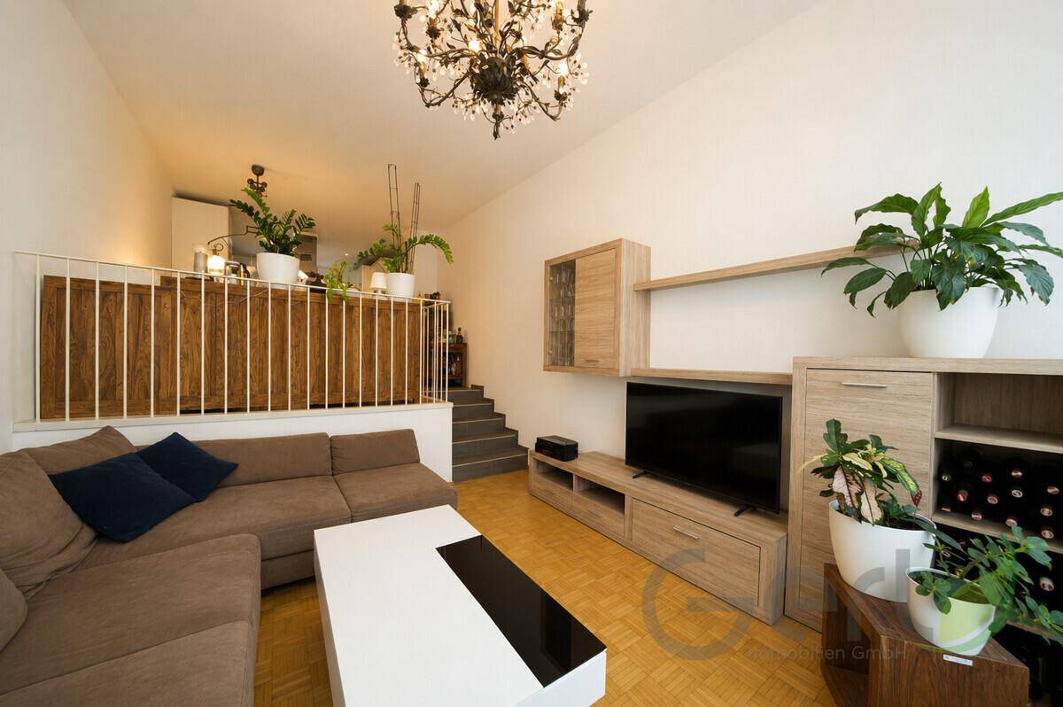 Heller Wohnbereich mit beigem Sofa, TV-Möbeln und einem dekorativen Kronleuchter.