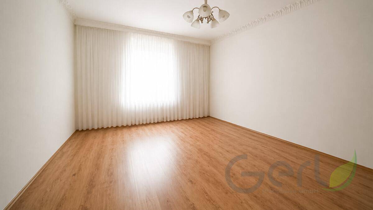 Leeres Zimmer mit hellem Laminatboden, weißen Wänden und einem großen Fenster für viel Tageslicht.