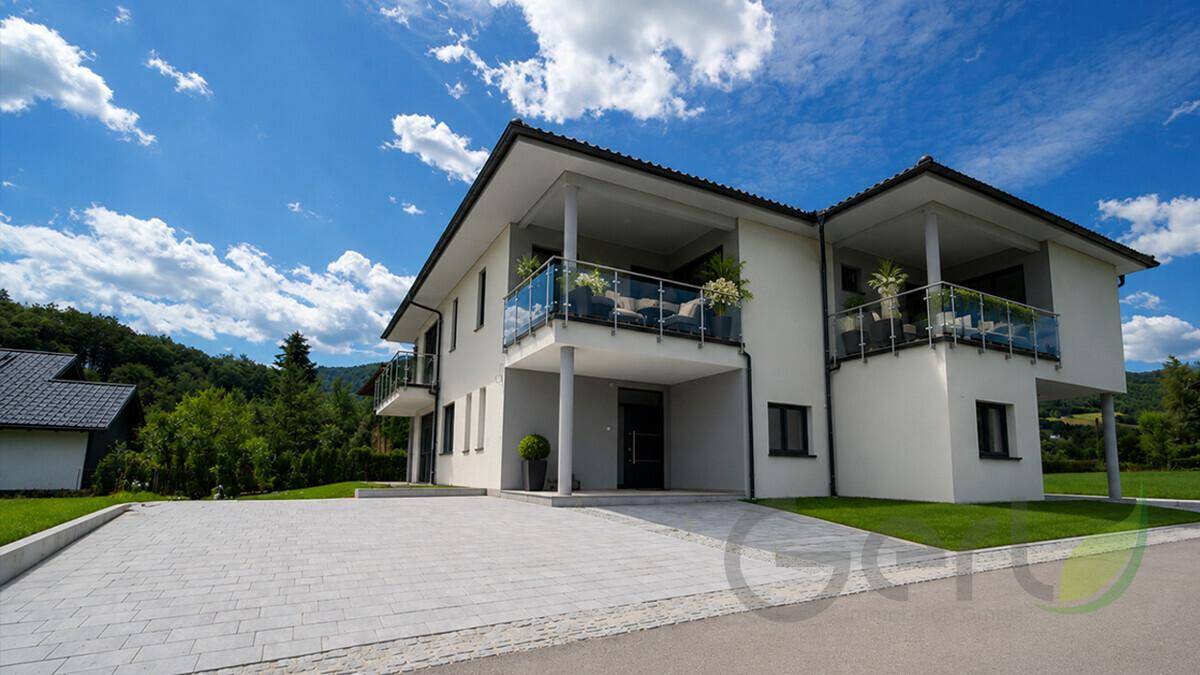 Moderne Hausfassade mit mehreren Balkonen und einer gepflasterten Auffahrt.