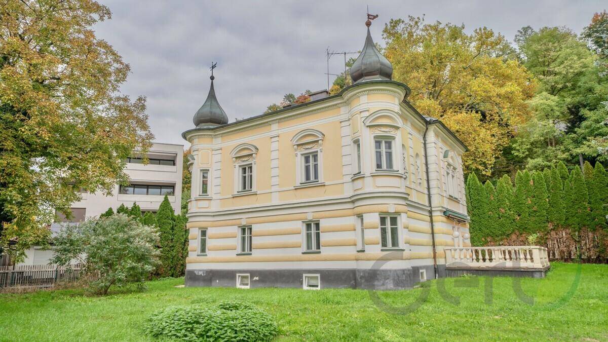 Historische Villa mit klassischer Architektur, umgeben von Bäumen und Grünflächen.