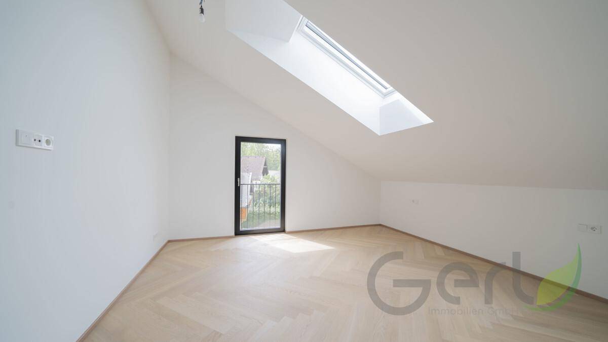 Helles Dachzimmer mit schrägen Wänden, großem Dachfenster und Zugang zu einem französischen Balkon.