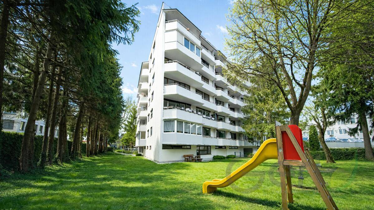 Grüner Gartenbereich mit Spielplatz und einem großen Wohngebäude im Hintergrund.