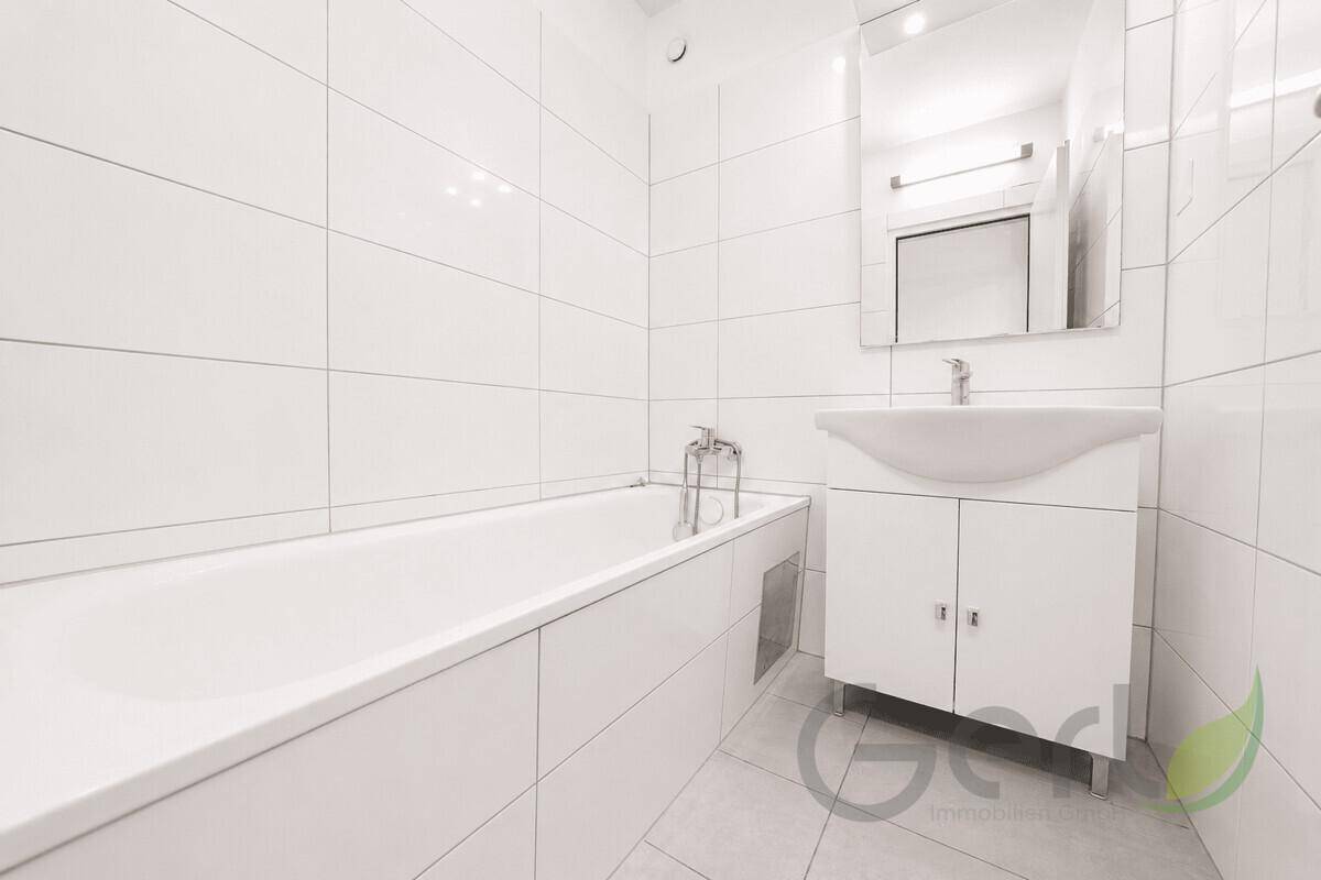 Modernes Badezimmer mit weißen Fliesen, Badewanne und Waschtisch mit Spiegel.