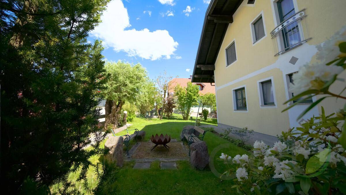 Idyllischer Gartenbereich mit Feuerstelle, Sitzgelegenheiten und blühenden Sträuchern, perfekt für Abende im Freien.