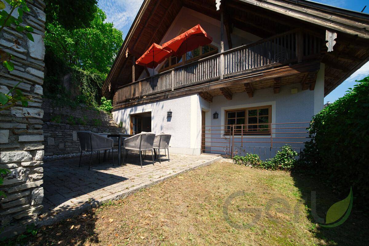 Terrasse mit Gartenmöbeln und Blick auf das traditionelle Haus mit Holzbalkon.