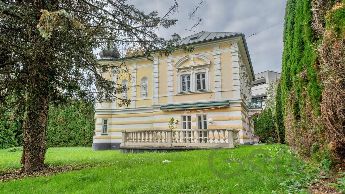 Seitenansicht der historischen Villa mit Balkon und weitläufigem Gartenbereich.