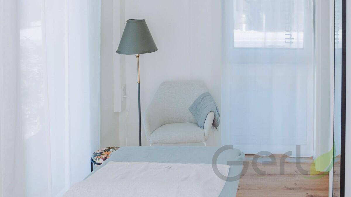 Gemütlicher Bereich im Behandlungsraum mit einem Sessel, Stehlampe und hellem Holzboden, umgeben von weißen Wänden.