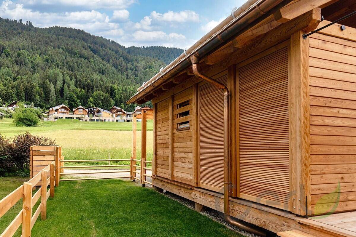 Rustikales Holzhaus mit Fensterläden und grüner Wiese im Hintergrund, umgeben von Natur.