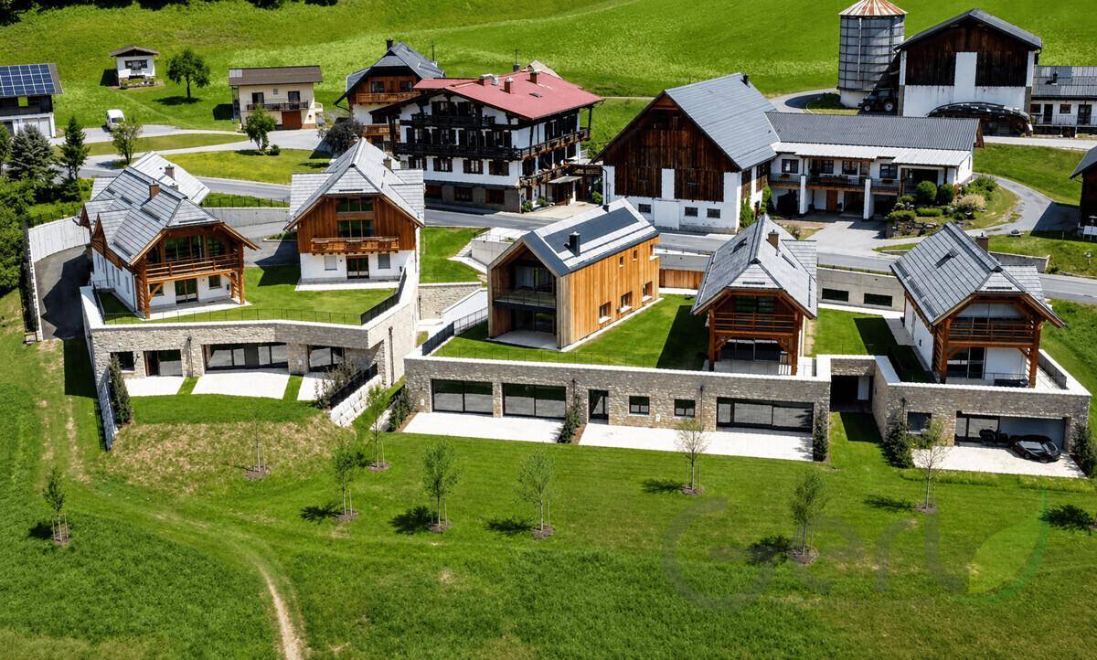 Luftaufnahme einer modernen Wohnsiedlung mit Häusern in alpiner Architektur und viel Grünfläche.
