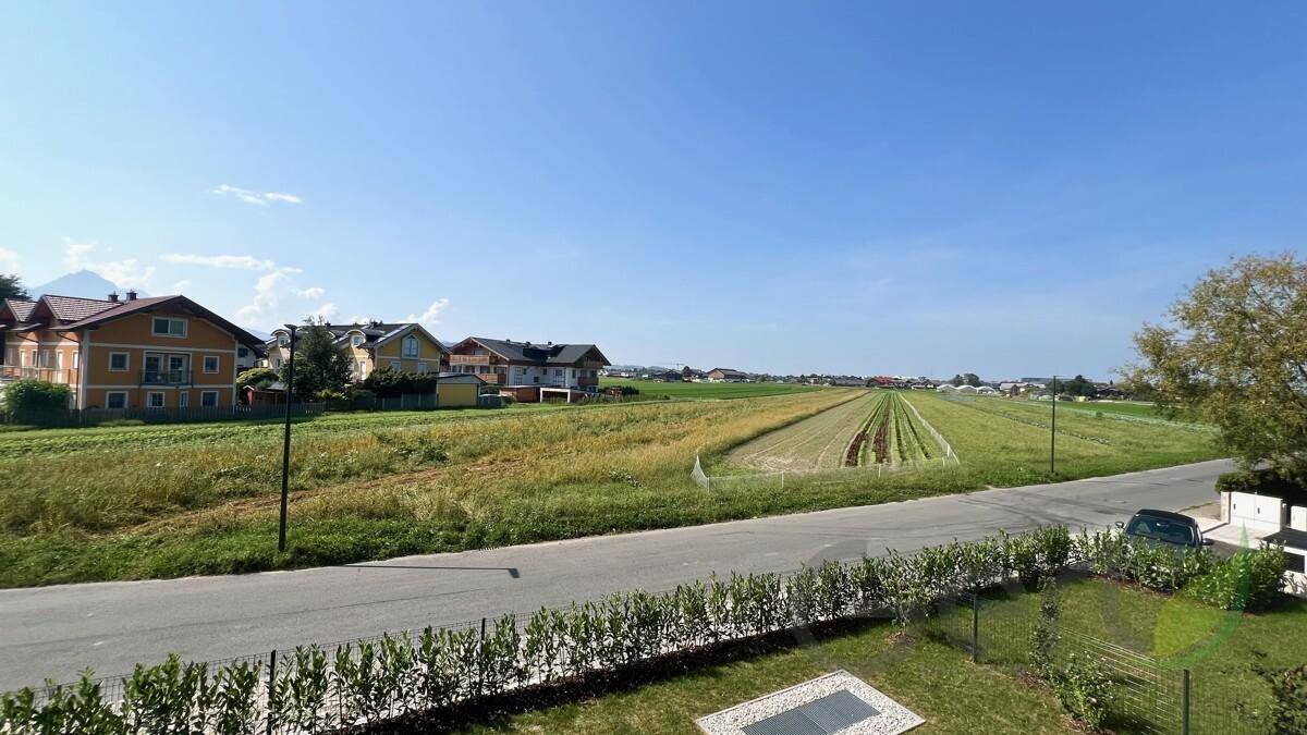 Weitläufiger Blick über grüne Felder und ländliche Umgebung mit Häusern am Horizont unter blauem Himmel.