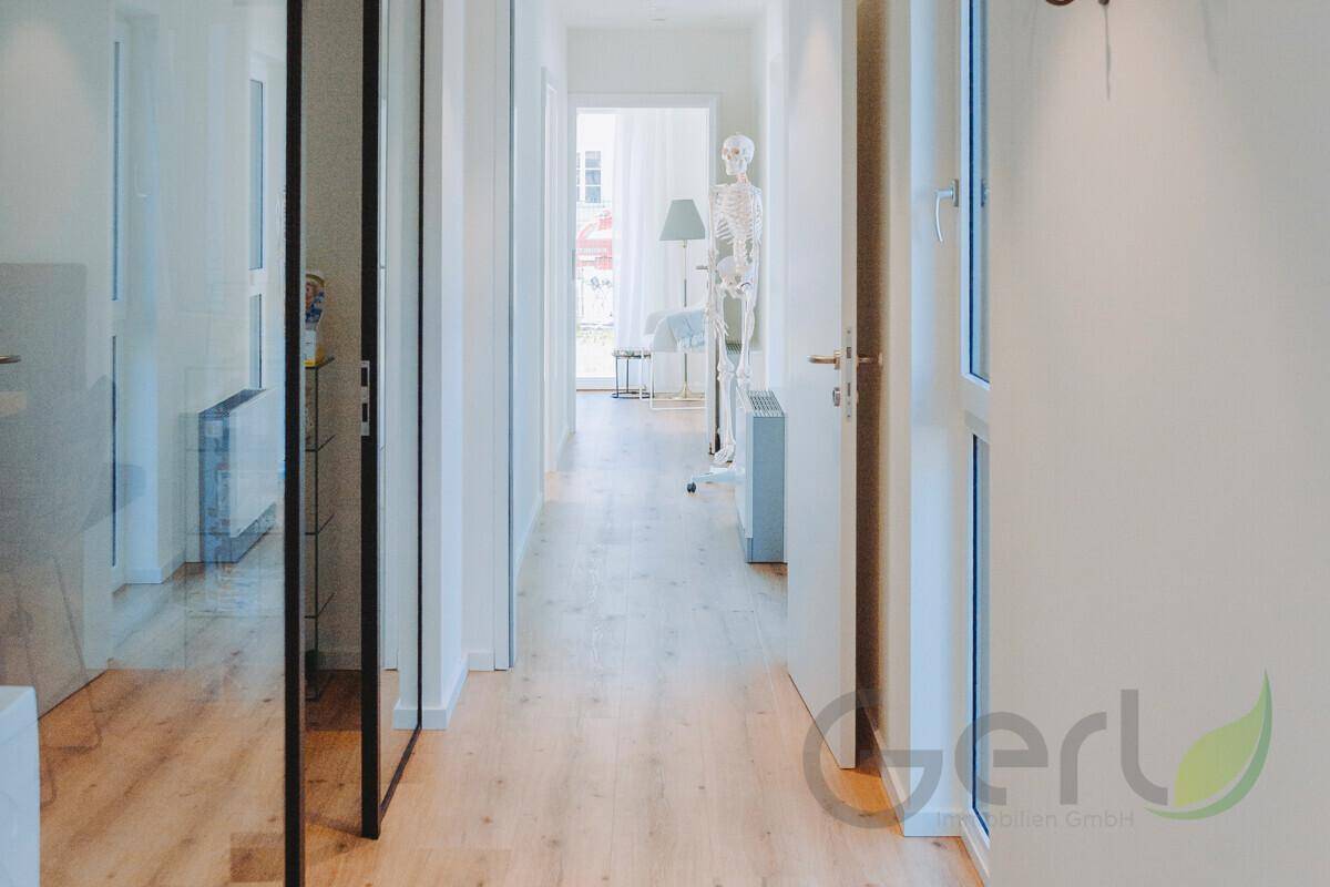 Heller Flur mit Holzboden und weißen Wänden, der zu weiteren Räumen führt und viel Tageslicht bietet.
