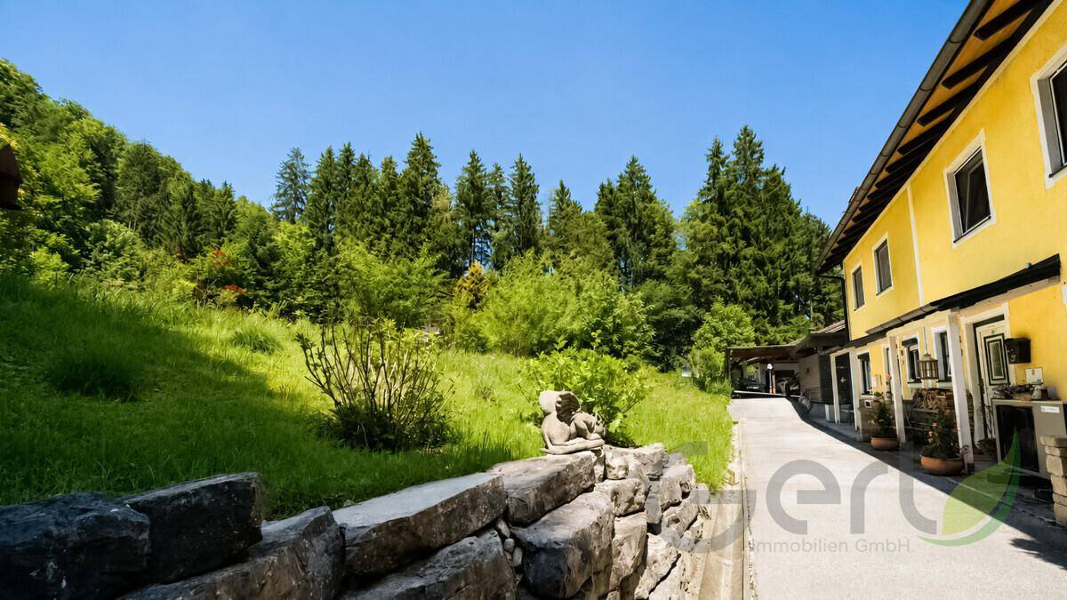 Gelbes Gebäude mit Steinmauer, Weg und grüner Hanglandschaft unter blauem Himmel.