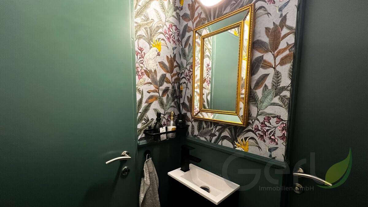 Stilvolles Gäste-WC mit auffälliger Tapete, modernem Waschbecken und goldenem Spiegelrahmen.