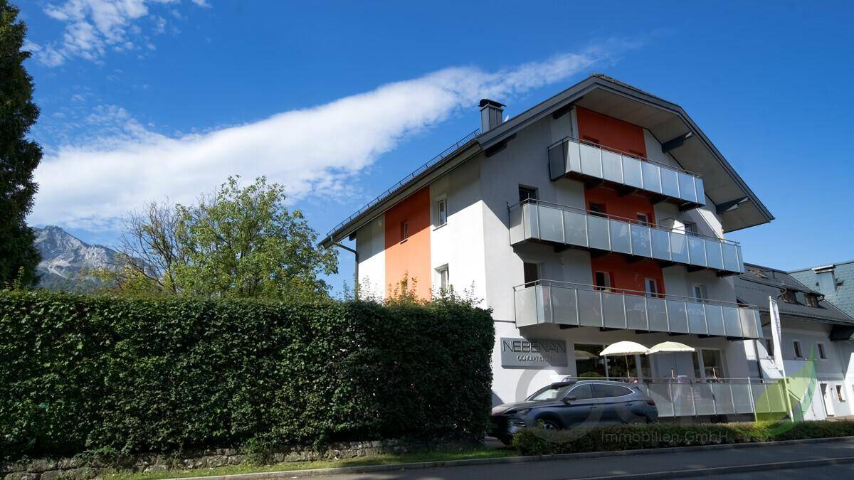 Modernes Gebäude mit Balkonen und orangefarbenen Akzenten, umgeben von einer grünen Hecke.