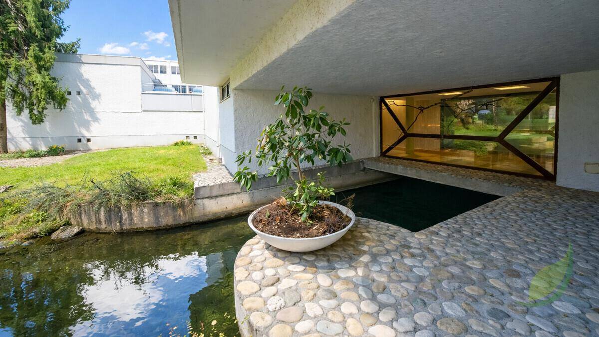 Architektonisches Detail mit einem Teich und einem gepflasterten Bereich am Gebäude.