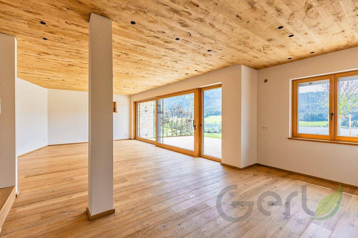Heller, leerer Wohnbereich mit Holzboden, Holzdecke und großen Fenstern zur Landschaft.