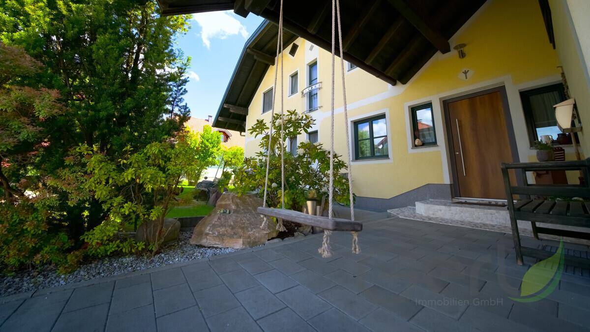 Eingangsbereich des Hauses mit gepflastertem Weg, üppigem Grün und einer charmanten Holzschaukel.